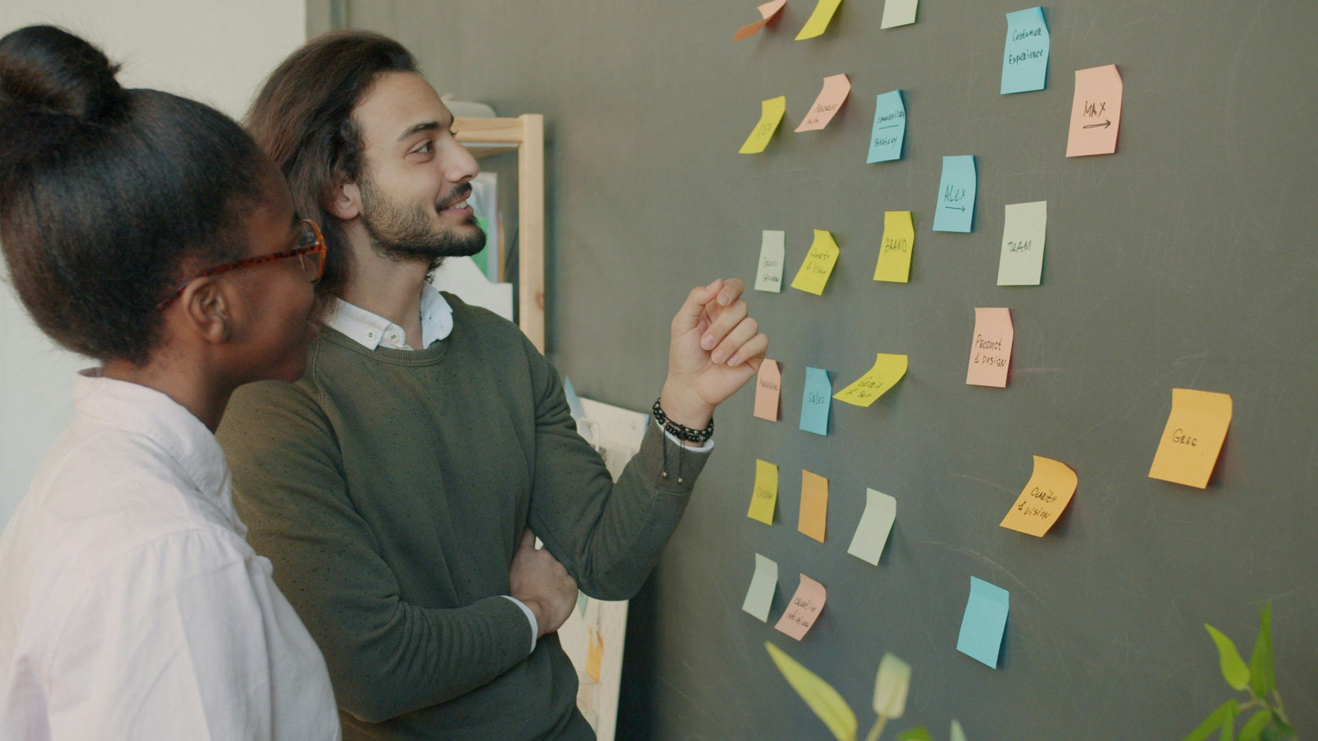 Two colleagues discussing ideas on sticky notes pinned to a wall